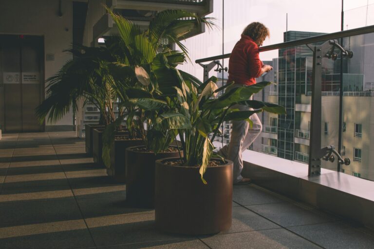 Person enjoying view from a modern balcony with lush potted plants, capturing urban architecture.